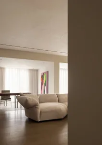 A modern living room with a beige sectional sofa, a dining area, and a colorful abstract painting on the wall.