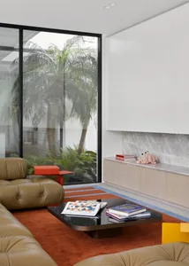 Modern living room with leather sofas, coffee table, books, and indoor plants, featuring a sleek black coffee table, bright o