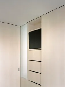 A modern minimalist closet featuring wooden drawers and a flat-screen television mounted within.