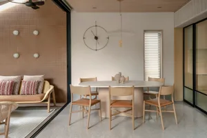 A minimalist dining room featuring a modern, round marble table surrounded by wooden chairs, with a clock on the wall and amb