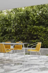 A modern outdoor seating area with yellow cushions on metal-framed chairs around a rectangular table.