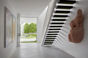 A modern staircase with metal railings and green carpeted steps leading up to a white wall with a large, abstract sculpture m