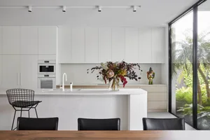 Modern kitchen with white cabinets and island, featuring a vase of flowers and large window.
