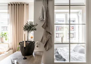 A minimalist bedroom featuring neutral-toned furniture, textiles, and decor, with a window providing natural light.