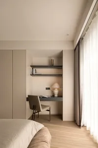 A minimalist bedroom featuring a neutral-color work area with a desk, chair, and lamp.