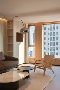 Interior view of a modern living room featuring wooden chairs, a leather sofa, marble and steel tables, and a steel floor lam