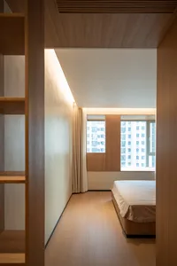 A minimalist bedroom with wooden flooring and a large window overlooking a cityscape.