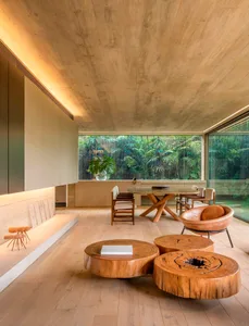 A modern living room with wooden furniture and large windows overlooking greenery.