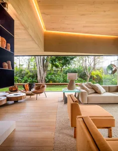 A spacious modern living room with wooden flooring, furniture, and ceiling, featuring a large window overlooking a garden.