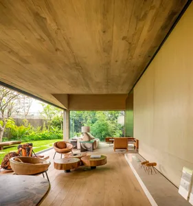 A modern living room with wooden furniture, concrete walls, and a glass door leading to a green outdoor space.