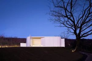 A minimalist residential exterior with concrete structure and large glass windows.