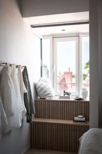Minimalist interior with wooden window bench, white cushions, and clothing hanging on a natural wood hook rack.