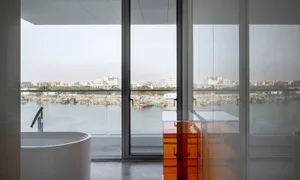 A modern bathroom featuring glass walls and a view of the city through large windows.
