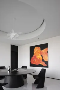 A minimalist design featuring black and white elements, a round table, black chairs, and a large goldfish artwork on the wall