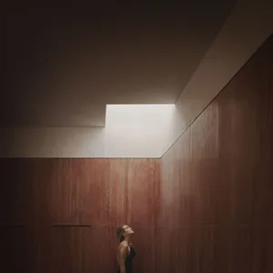 A minimalist interior designed with concrete materials, featuring a person looking upwards towards a skylight.