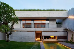 A modern residential building with a concrete exterior, glass windows, and a rooftop garden.