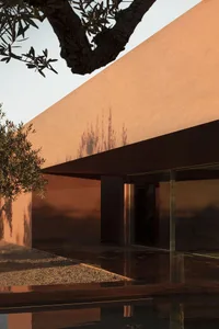 Modern exterior view of a house with red terrazzo and olive tree shadows on the wall.