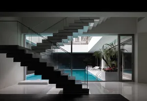 Modern home interior featuring a minimalist staircase with glass railings and black marble steps, overlooking a pool area wit