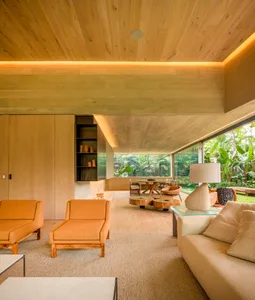 Modern living room interior with wooden floors, walls, and ceiling, featuring orange furniture and a glass coffee table.