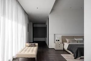 Modern bedroom with neutral decor, featuring a minimalist bed and a beige lounge chair.