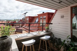 A modern rooftop balcony featuring a concrete bench, white stools, and potted plants.