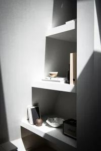A minimalist shelf with white shelves and wooden elements, featuring simple decor items.