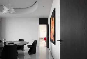 A modern dining room featuring a circular table with black chairs, located near a black door with decorative handles and an o