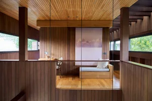 A minimalist living room with wooden walls, floor, and ceiling, featuring a small couch and a large window.