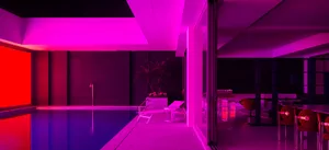 A modern interior space featuring a pool-side deck illuminated by vibrant purple lighting.