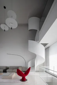 A modern residential interior featuring a minimalist design with a spiral staircase, red chair, and white interior.