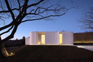 A modern house with white curved panels illuminated at dusk.