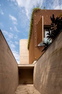 Modern exterior of a building with wooden deck and green plants on the roof, against a blue sky with white clouds.