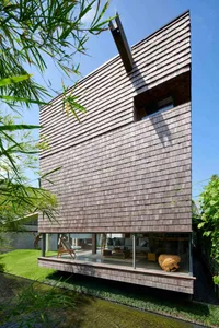 A modern holiday villa with a wooden exterior and glass windows overlooking lush greenery.