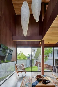 A modern living room with concrete floors, wooden furniture, and glass windows overlooking a garden.