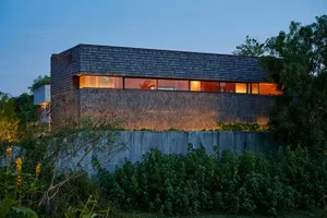 A modern residential house with a wooden exterior at night, illuminated windows.