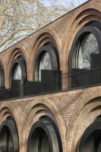 Modern brick arches with black railings and trees in the background.