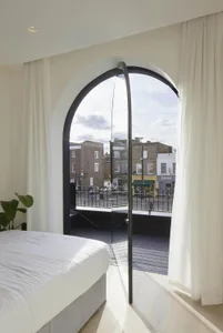 A modern bedroom features a glass window overlooking a residential area.