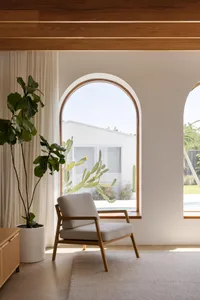 A minimalist living room with a concrete floor and arched windows, featuring a comfortable armchair and a large potted plant.