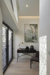 A modern entryway featuring wooden flooring and metal accents, with a desk, chair, and framed artwork.