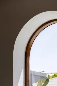 Close-up of an arched window with a wooden frame and concrete sill, set against a brown wall.