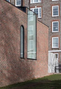 Modern brick exterior of a building with large glass window and arched glass window on stairs.