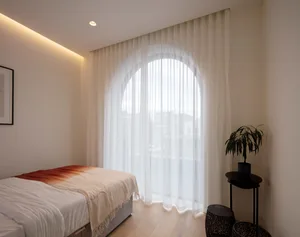 Modern minimalist bedroom featuring a bed with white bedding and sheer white curtains, minimalistic decor, and a small round