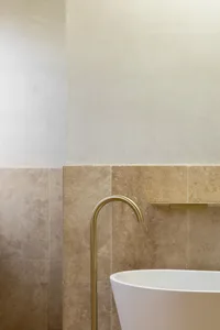 A minimalist bathroom with beige tiles and a white bathtub.