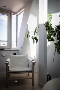 A modern interior featuring a white upholstered chair with wooden arms and legs, positioned near a window.