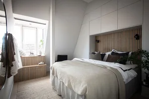 A minimalist bedroom featuring a wooden headboard, white linens, and a window seat.