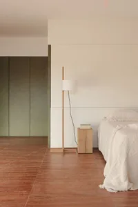 A minimalist bedroom featuring wooden furniture and a floor lamp.