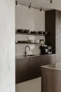 Minimalist kitchen with dark wood cabinets, marble countertop, and black faucet.