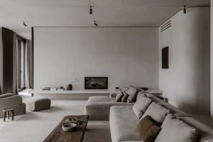 A minimalist living room featuring concrete walls, a large sectional sofa, and a low-profile coffee table.