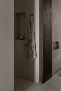 A minimalist bathroom with concrete walls, a towel hanging on the wall, and a built-in shelf.