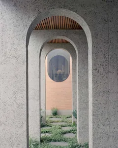 A modern architectural entrance with a textured concrete wall featuring a circular window and an arched doorway.
